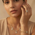 Woman wearing gold jewelry including a necklace, bracelet, and ring on a beige background