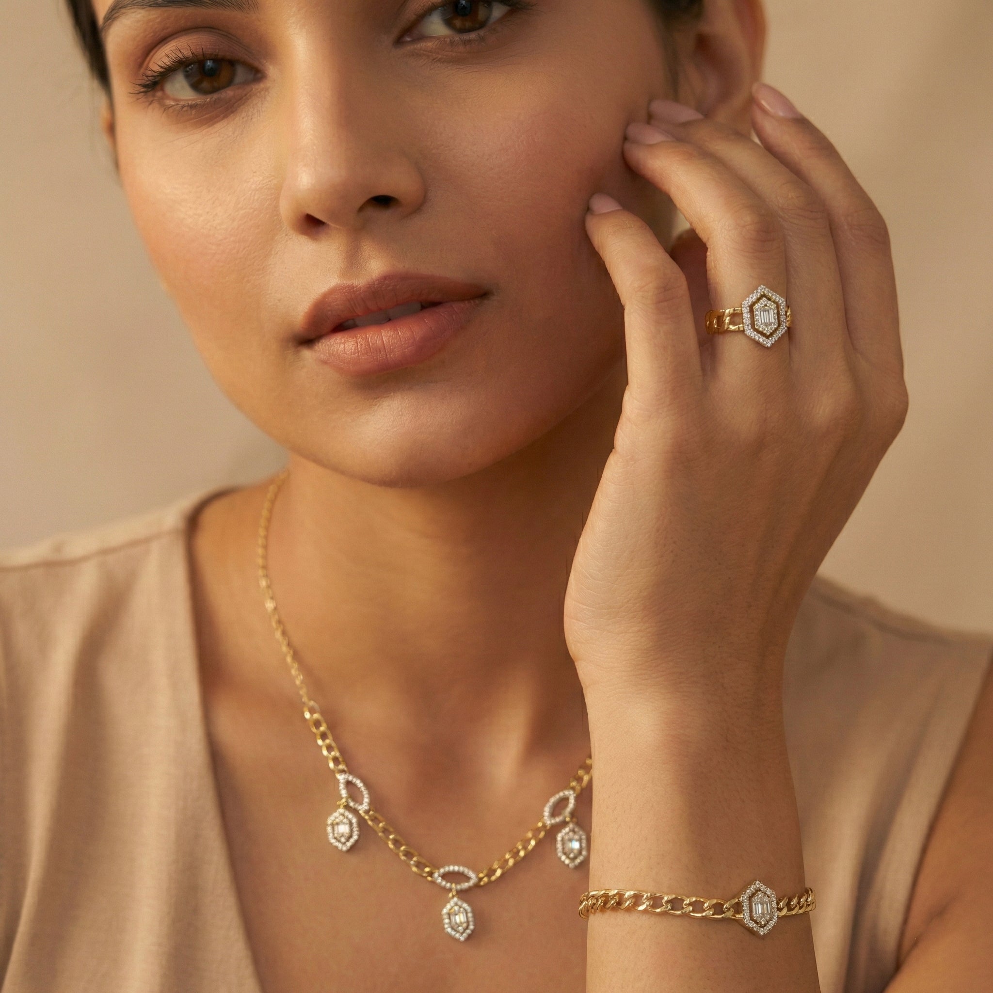 Woman wearing gold jewelry including a necklace, bracelet, and ring on a beige background