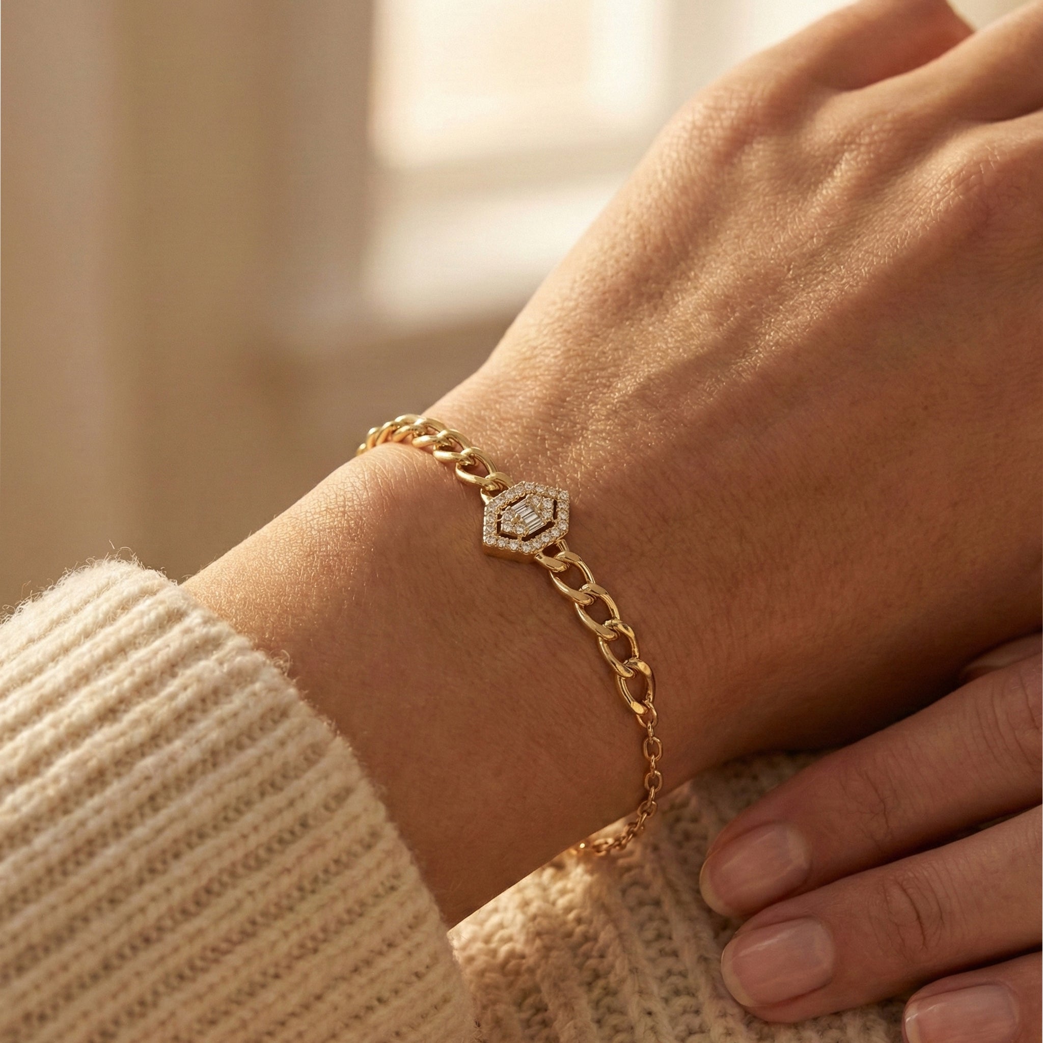 Gold bracelet with a hexagonal design on a wrist, wearing a beige sweater.