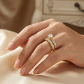Hand wearing a gold ring with a diamond on a soft fabric background
