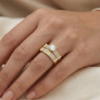 Gold ring with a diamond on a person's finger against a beige background