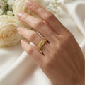 Hand wearing a gold ring with white roses in the background