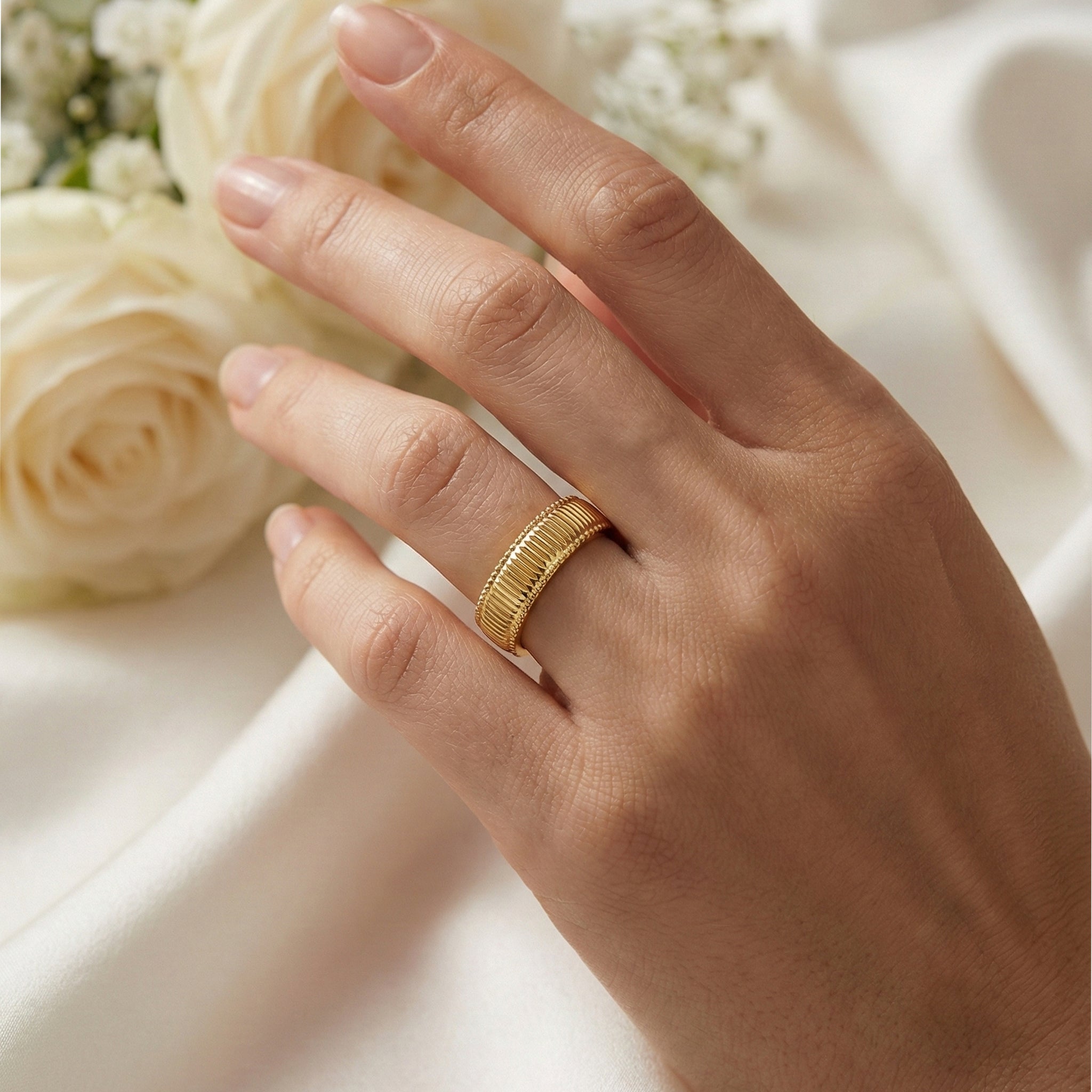 Hand wearing a gold ring with white roses in the background