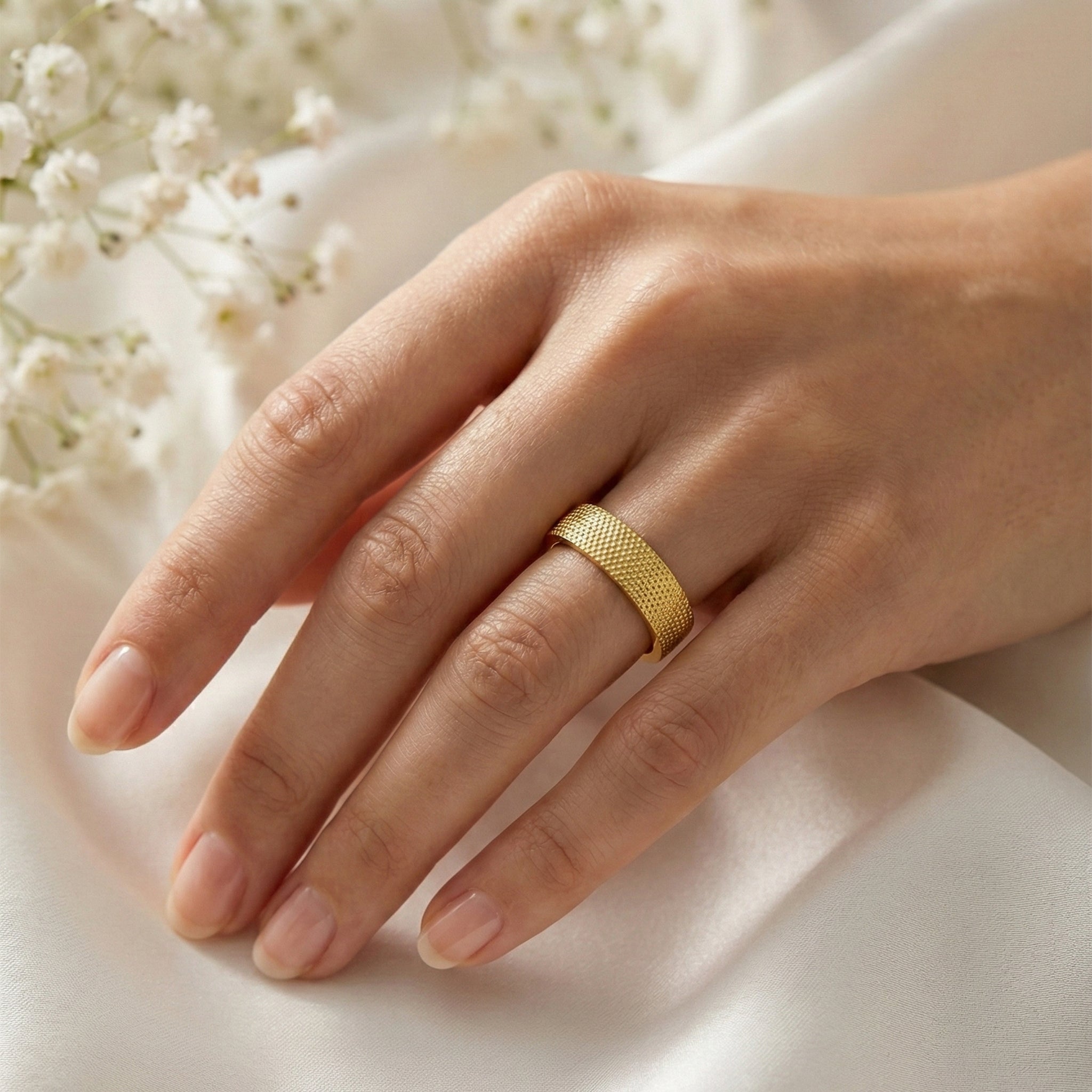 Hand wearing a gold ring with a soft white background