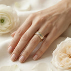 Hand wearing a gold ring with white flowers in the background