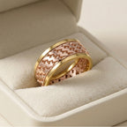 Two gold and rose gold rings with intricate patterns on a beige cushion in a jewelry box.