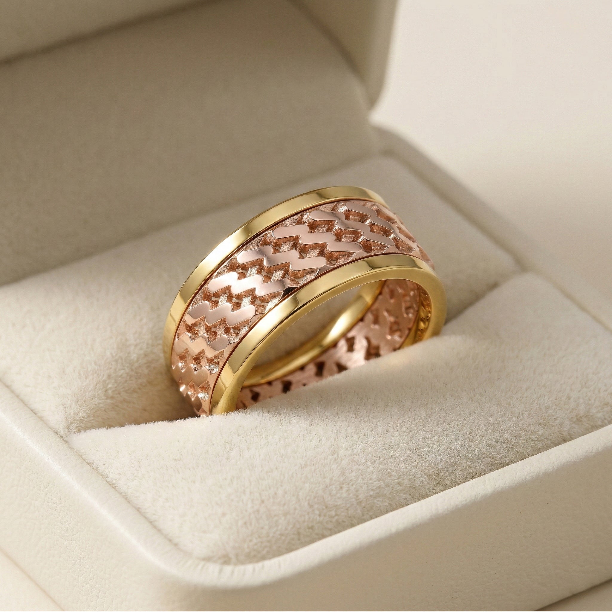 Two gold and rose gold rings with intricate patterns on a beige cushion in a jewelry box.